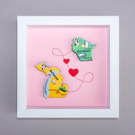 Framed artwork with colorful state shapes of Michigan and Wisconsin on a pink background.